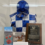 A display case showing a blue and white checkered jockey robe on a mannequin torso, with a Kentucky Horse card, a framed Secretariat plaque, at the Albany International Airport